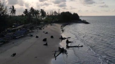 Güneşin kumsaldaki kumları yıkayan deniz dalgalarının üzerinde battığı güzel bir an. Doğu Aceh, Endonezya 'da bozulmamış bir sahilde gün batımının sinematik drone görüntüleri.
