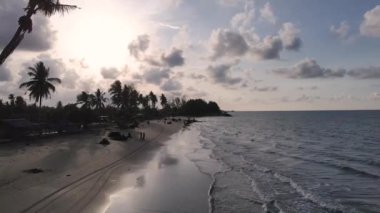 Güneşin kumsaldaki kumları yıkayan deniz dalgalarının üzerinde battığı güzel bir an. Doğu Aceh, Endonezya 'da bozulmamış bir sahilde gün batımının sinematik drone görüntüleri.