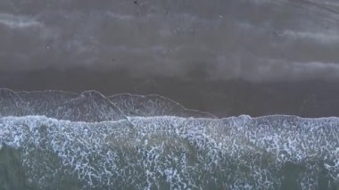 Güneşin kumsaldaki kumları yıkayan deniz dalgalarının üzerinde battığı güzel bir an. Doğu Aceh, Endonezya 'da bozulmamış bir sahilde gün batımının sinematik drone görüntüleri.
