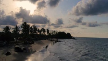 Güneşin kumsaldaki kumları yıkayan deniz dalgalarının üzerinde battığı güzel bir an. Doğu Aceh, Endonezya 'da bozulmamış bir sahilde gün batımının sinematik drone görüntüleri.