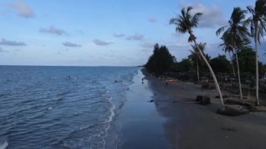 Güneşin kumsaldaki kumları yıkayan deniz dalgalarının üzerinde battığı güzel bir an. Doğu Aceh, Endonezya 'da bozulmamış bir sahilde gün batımının sinematik drone görüntüleri.