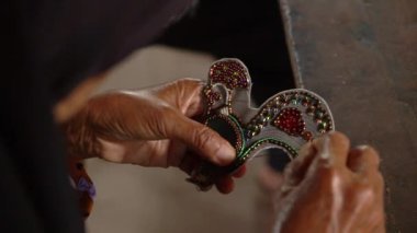 El yapımı mücevher yapma süreci. Asyalı yaşlı bir kadının elleri atölyedeki ahşap masada el yapımı mücevherler, boncuklar ve bilezikler yapıyor. Yakın çekim ve ağır çekim.