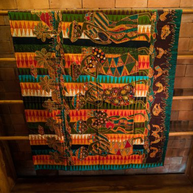Uzun ahşap raflarda, üzerinde ince detaylar bulunan geleneksel Java kumaşlarından çarşaflar asılı. Bu batik kumaş çarşaflar çeşitli motif ve renklere sahip profesyonel zanaatkarlar tarafından çizilmiş.