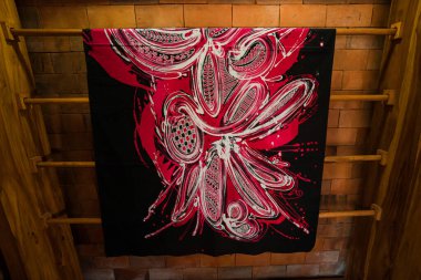 Uzun ahşap raflarda, üzerinde ince detaylar bulunan geleneksel Java kumaşlarından çarşaflar asılı. Bu batik kumaş çarşaflar çeşitli motif ve renklere sahip profesyonel zanaatkarlar tarafından çizilmiş.