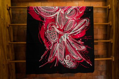 Uzun ahşap raflarda, üzerinde ince detaylar bulunan geleneksel Java kumaşlarından çarşaflar asılı. Bu batik kumaş çarşaflar çeşitli motif ve renklere sahip profesyonel zanaatkarlar tarafından çizilmiş.