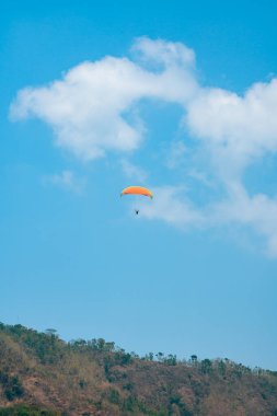 Dağlık bölgelerde ve açık mavi gökyüzünde uçan paraglasyon cazibesi. Paragliding, gökyüzünde paraşütle uçarak adrenalin salgılayan bir spordur.
