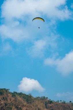 Dağlık bölgelerde ve açık mavi gökyüzünde uçan paraglasyon cazibesi. Paragliding, gökyüzünde paraşütle uçarak adrenalin salgılayan bir spordur.