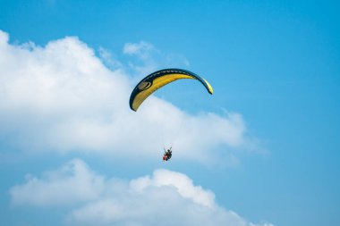 Adrenalin salgılayan bir ekstrem spor, açık mavi gökyüzüne karşı yamaç paraşütü. Gökyüzünde paraşütüyle uçan paraşütçü. Arka planda mavi gökyüzü ve güneşli bir günde beyaz bulutlar..