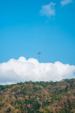 Dağlık bölgelerde ve açık mavi gökyüzünde uçan paraglasyon cazibesi. Paragliding, gökyüzünde paraşütle uçarak adrenalin salgılayan bir spordur.