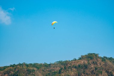 Dağlık bölgelerde ve açık mavi gökyüzünde uçan paraglasyon cazibesi. Paragliding, gökyüzünde paraşütle uçarak adrenalin salgılayan bir spordur.