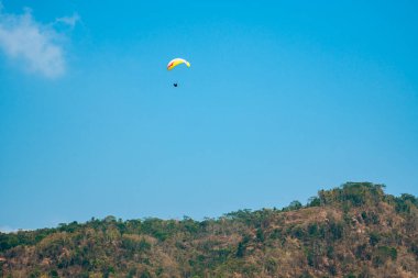 Dağlık bölgelerde ve açık mavi gökyüzünde uçan paraglasyon cazibesi. Paragliding, gökyüzünde paraşütle uçarak adrenalin salgılayan bir spordur.