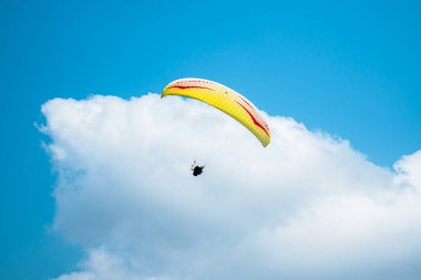 Adrenalin salgılayan bir ekstrem spor, açık mavi gökyüzüne karşı yamaç paraşütü. Gökyüzünde paraşütüyle uçan paraşütçü. Arka planda mavi gökyüzü ve güneşli bir günde beyaz bulutlar..