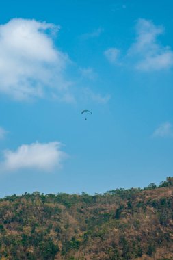 Dağlık bölgelerde ve açık mavi gökyüzünde uçan paraglasyon cazibesi. Paragliding, gökyüzünde paraşütle uçarak adrenalin salgılayan bir spordur.