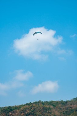 Dağlık bölgelerde ve açık mavi gökyüzünde uçan paraglasyon cazibesi. Paragliding, gökyüzünde paraşütle uçarak adrenalin salgılayan bir spordur.