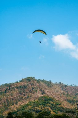 Dağlık bölgelerde ve açık mavi gökyüzünde uçan paraglasyon cazibesi. Paragliding, gökyüzünde paraşütle uçarak adrenalin salgılayan bir spordur.