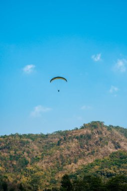 Dağlık bölgelerde ve açık mavi gökyüzünde uçan paraglasyon cazibesi. Paragliding, gökyüzünde paraşütle uçarak adrenalin salgılayan bir spordur.