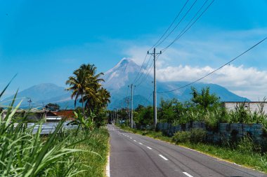 Merapi Dağı 'nın güzelliği, önündeki otoyol ve elektrik direkleriyle çok net bir şekilde görülebilir. Sıcak bir günde Merapi Dağı 'nın ihtişamı. Arka planda mavi gökyüzü var.