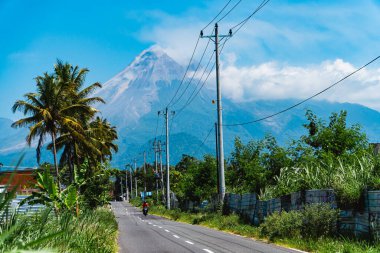 Merapi Dağı 'nın güzelliği, önündeki otoyol ve elektrik direkleriyle çok net bir şekilde görülebilir. Sıcak bir günde Merapi Dağı 'nın ihtişamı. Arka planda mavi gökyüzü var.