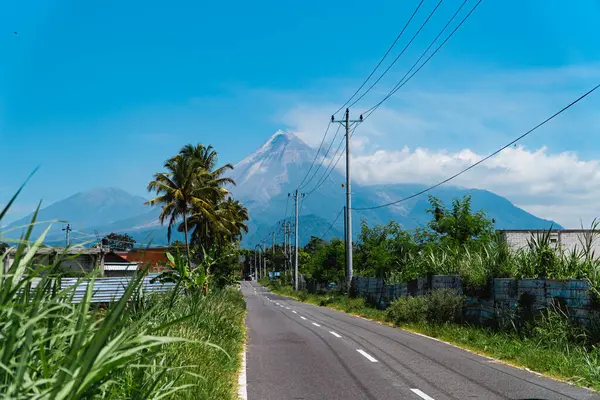 Merapi Dağı 'nın güzelliği, önündeki otoyol ve elektrik direkleriyle çok net bir şekilde görülebilir. Sıcak bir günde Merapi Dağı 'nın ihtişamı. Arka planda mavi gökyüzü var.