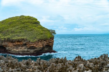 Keskin mercan kayalarıyla dolu tepeler denizin ortasında küçük bir adayla mavi denizi sınırlıyor. Sahildeki mercan tepeleri ve arka planda çok güzel mavi bir deniz.