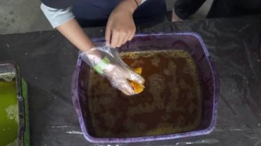 Geleneksel batik kumaşı boyamayı öğrenen öğrencilerin havuza boya bandırıp kaynar suya batırdıkları 4K 'lık görüntüleri kapatın. Yeni başlayanlar batik kumaşı geleneksel şekilde boyamayı öğrenirler.