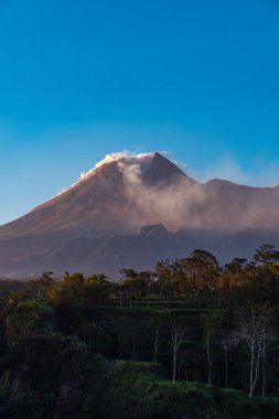 Karanlık çökmeden Merapi Dağı 'nın güzelliği ve önünde soğuk lav uçurumu var. Merapi Dağı açık bir günde mavi gökyüzü ve yanında bulutlarla detaylı görünüyor.