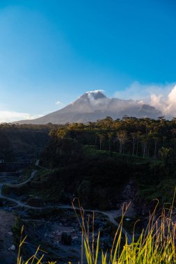 Karanlık çökmeden Merapi Dağı 'nın güzelliği ve önünde soğuk lav uçurumu var. Merapi Dağı açık bir günde mavi gökyüzü ve yanında bulutlarla detaylı görünüyor.