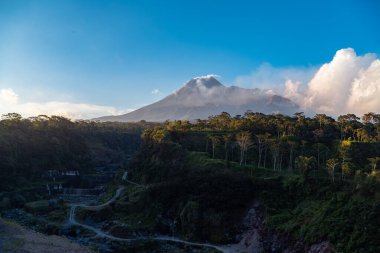 Karanlık çökmeden Merapi Dağı 'nın güzelliği ve önünde soğuk lav uçurumu var. Merapi Dağı açık bir günde mavi gökyüzü ve yanında bulutlarla detaylı görünüyor.