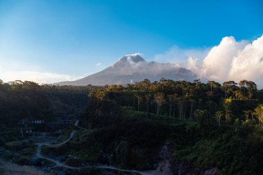 Karanlık çökmeden Merapi Dağı 'nın güzelliği ve önünde soğuk lav uçurumu var. Merapi Dağı açık bir günde mavi gökyüzü ve yanında bulutlarla detaylı görünüyor.