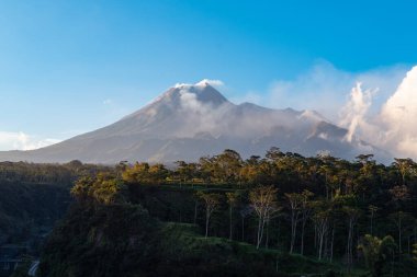 Karanlık çökmeden Merapi Dağı 'nın güzelliği ve önünde soğuk lav uçurumu var. Merapi Dağı açık bir günde mavi gökyüzü ve yanında bulutlarla detaylı görünüyor.