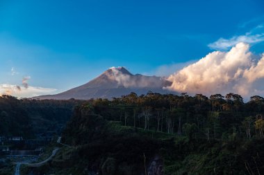 Karanlık çökmeden Merapi Dağı 'nın güzelliği ve önünde soğuk lav uçurumu var. Merapi Dağı açık bir günde mavi gökyüzü ve yanında bulutlarla detaylı görünüyor.