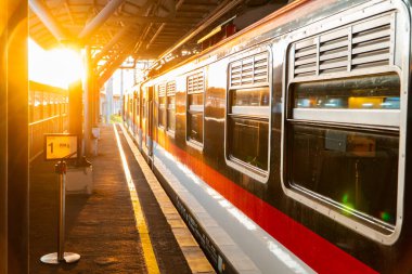 Günbatımının altın ışığı Yogyakarta tren istasyonunu aydınlatır. Tren istasyonda duruyor, batan güneş vagona yansıyor.