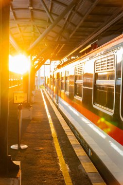 Günbatımının altın ışığı Yogyakarta tren istasyonunu aydınlatır. Tren istasyonda duruyor, batan güneş vagona yansıyor.