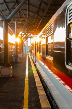 Günbatımının altın ışığı Yogyakarta tren istasyonunu aydınlatır. Tren istasyonda duruyor, batan güneş vagona yansıyor.