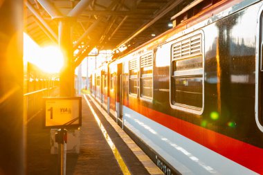 Günbatımının altın ışığı Yogyakarta tren istasyonunu aydınlatır. Tren istasyonda duruyor, batan güneş vagona yansıyor.