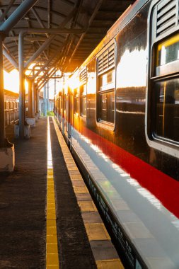 Günbatımının altın ışığı Yogyakarta tren istasyonunu aydınlatır. Tren istasyonda duruyor, batan güneş vagona yansıyor.