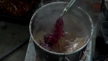 Katılımcıların geleneksel batik kumaşı boyamayı öğrenirken havuza boya bandırıp kaynar suya batırdıkları yavaş çekim görüntüleri. Yeni başlayanlar batik kumaşı geleneksel şekilde boyamayı öğrenirler.