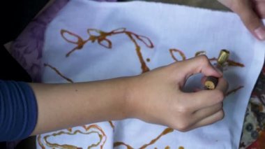 Geleneksel Batik yapmayı öğrenen katılımcıların yavaş çekim görüntüleri kızgın bir tavada kaydedilen sıcak balmumuyla canting medyasını kullanarak beyaz bir bez parçasına çizilmiş.