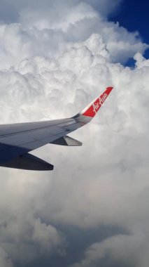 Ticari bir uçak penceresinden beyaz bulutlu mavi bir gökyüzü görüntüsü. Uçak kanatları, ticari bir uçağın penceresinin arkasından bulutların arasında sorunsuzca hareket ediyor.