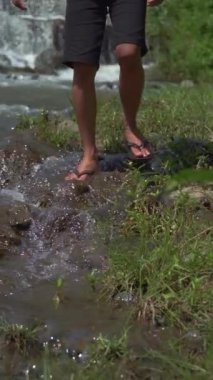 Temiz bir nehrin kenarında tek başına yürüyen bir Yürüyüşçü 'nün ayaklarına yakın dur. Erkek bir maceraperest, kayaların üzerinde sandaletle ve akan suyla nehrin kenarında yürüyor.
