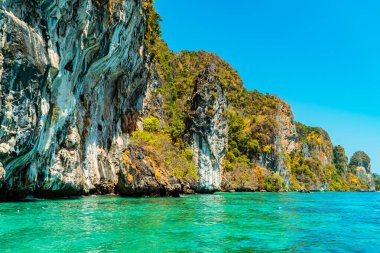 Yeşil ağaçlarla kaplı büyük kaya kayalıkları doğrudan Andaman Denizi 'ne bakıyor. Kayalık ve okyanus manzarası Tayland 'ın Phi-phi Adası' ndaki tropikal turizmin bir simgesidir.