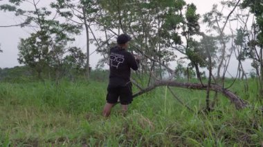 Bir adamın tepenin üzerine çarşaf dikme süreci. Ormanın ortasında, Merapi Dağı 'nın göz kamaştırıcı zemininde yalnız bir adam çiselemeden korunmak için bir çarşaf hazırlıyor..
