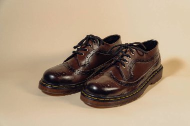 Close up of dark brown gradient wingtip shoes with rubber outsole made of genuine cowhide. Studio shot of an elegant and shiny vintage shoes product on a beige background clipart