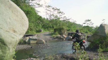 4k footage Crossing a river full of rocks on a dirt bike. outdoor activity driving through nature. Dirt bike riders cross a river with rocks and gushing water