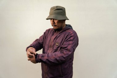 Half body portrait of mature Asian man with beard and mustache posing in ready style before traveling. Mature man wearing adventure outfit with jacket and bucket hat isolated on beige background.