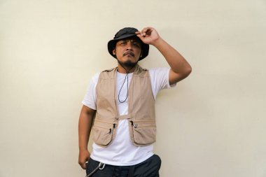 Sakallı ve bıyıklı, bej arka planda safari kıyafeti giyen, maço, olgun bir adam. Yetişkin bir Güneydoğu Asyalı 'nın yarı vücut portresi. Çeşitli pozlar veriyor. Yelek ve kova şapka takıyor.