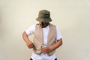 Sakallı ve bıyıklı, bej arka planda safari kıyafeti giyen, maço, olgun bir adam. Yetişkin bir Güneydoğu Asyalı 'nın yarı vücut portresi. Çeşitli pozlar veriyor. Yelek ve kova şapka takıyor.