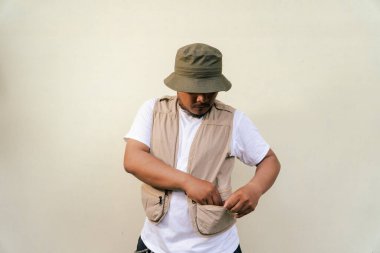 Sakallı ve bıyıklı, bej arka planda safari kıyafeti giyen, maço, olgun bir adam. Yetişkin bir Güneydoğu Asyalı 'nın yarı vücut portresi. Çeşitli pozlar veriyor. Yelek ve kova şapka takıyor.