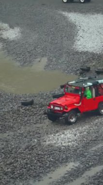 4K portre görüntüleri bir off-road turist cipinin su her yöne sıçrayıp yolcuları Merapi Dağı eteklerinde lav turuna çıkarana kadar yüksek hızda nehirden geçişini gösteriyor.