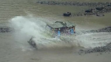 Bir off-road turist cipinin 4K görüntüsü yüksek hızda nehri geçerken su tüm yönlere sıçrayıp yolcuları Merapi Dağı eteklerindeki lav turunda ıslatırken görülüyor.